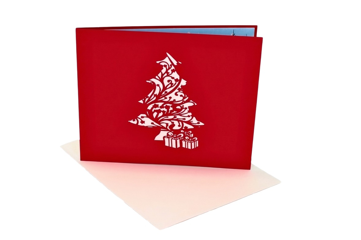 Rote Weihnachtskarte mit weiß ausgeschnittenem Weihnachtsbaum und Geschenken, davor ein cremefarbener Umschlag